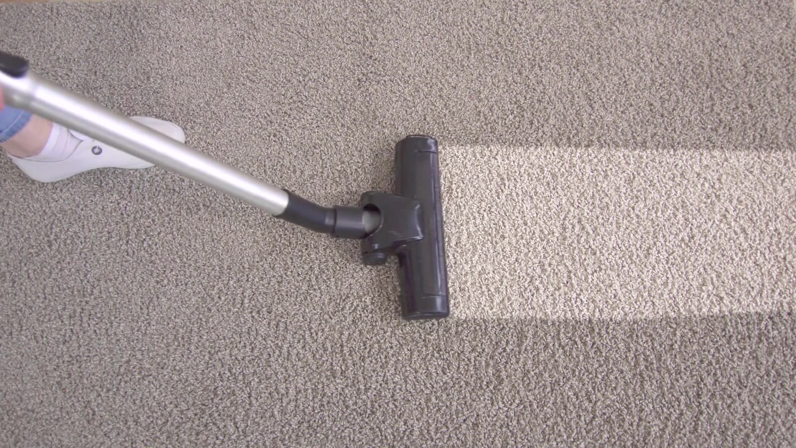 Vacuuming beige wall-to-wall carpet, with a cleaner, lighter stripe running across the room