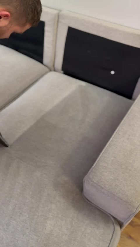 Good Day Cleaners technician cleaning the seat of a gray modular sectional, with a clean stripe showing next to the corner section